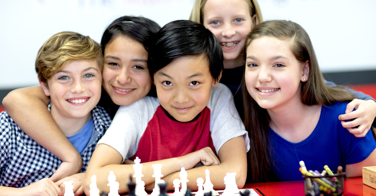 A diverse group of children next to a chess board.
