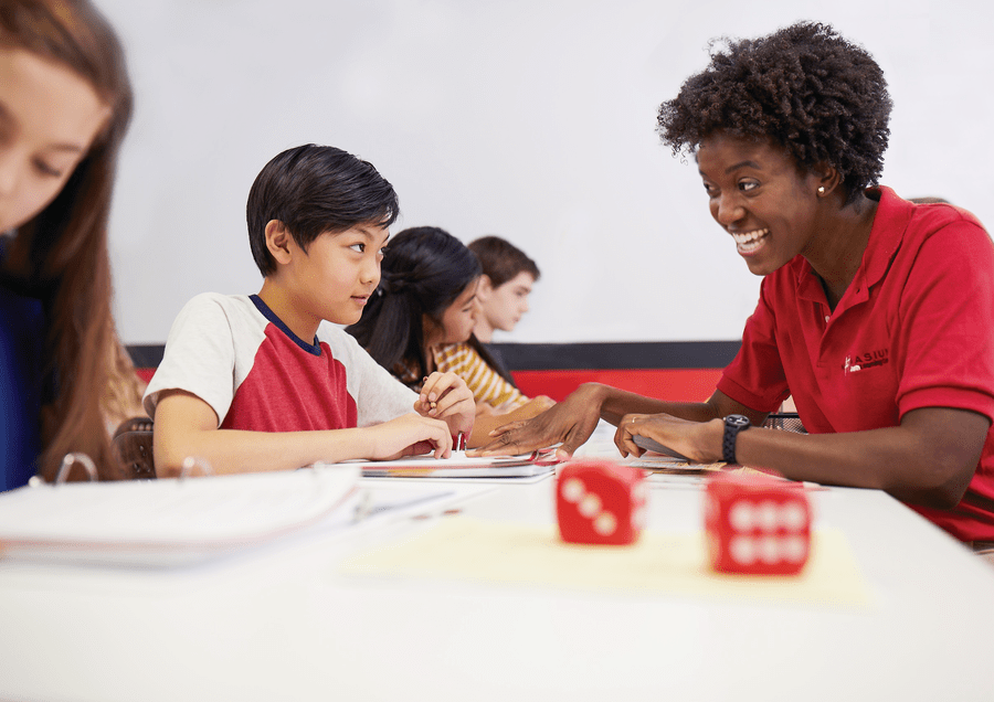 Image of a Mathnasium tutor helping a young student solve a math problem, with an unfocused view of dice on the table.