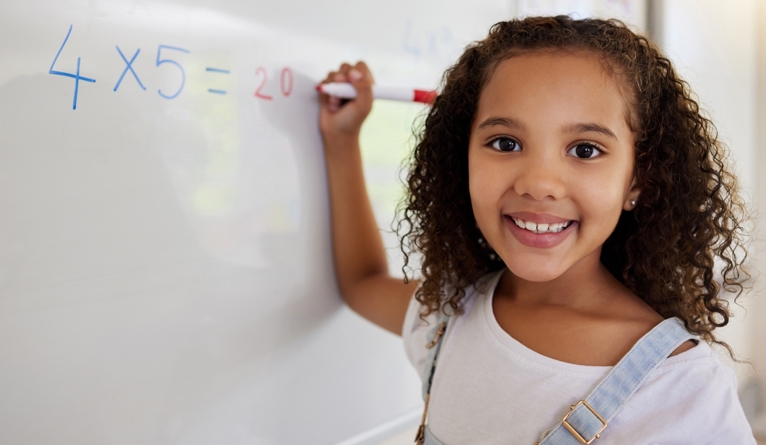 Elementary school girl smiling while writing a multiplication product on the whiteboard