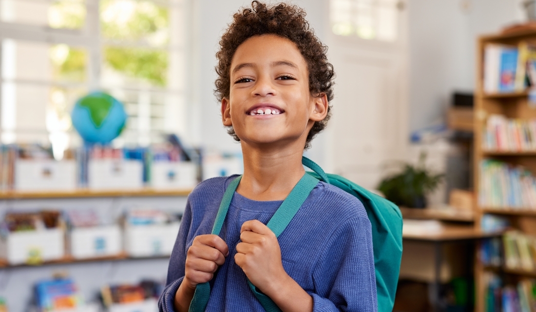 Confident elementary school student smiling with a backpack in a classroom, representing a positive attitude and growth mindset in math learning