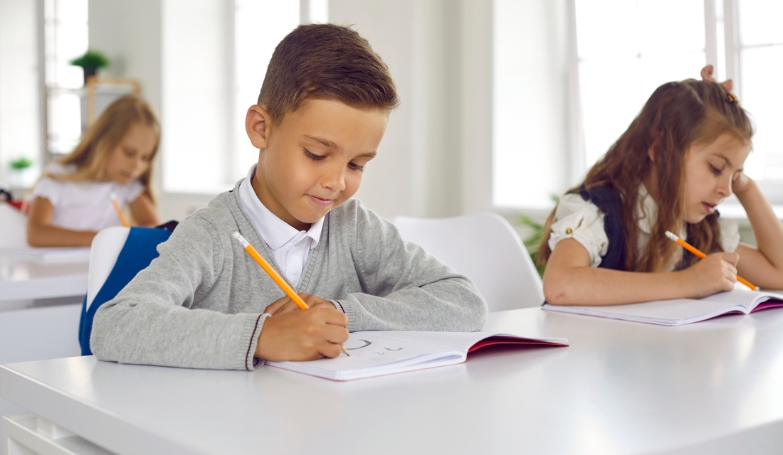 Young students working on math assignments at their desks, one appearing focused while another looks frustrated