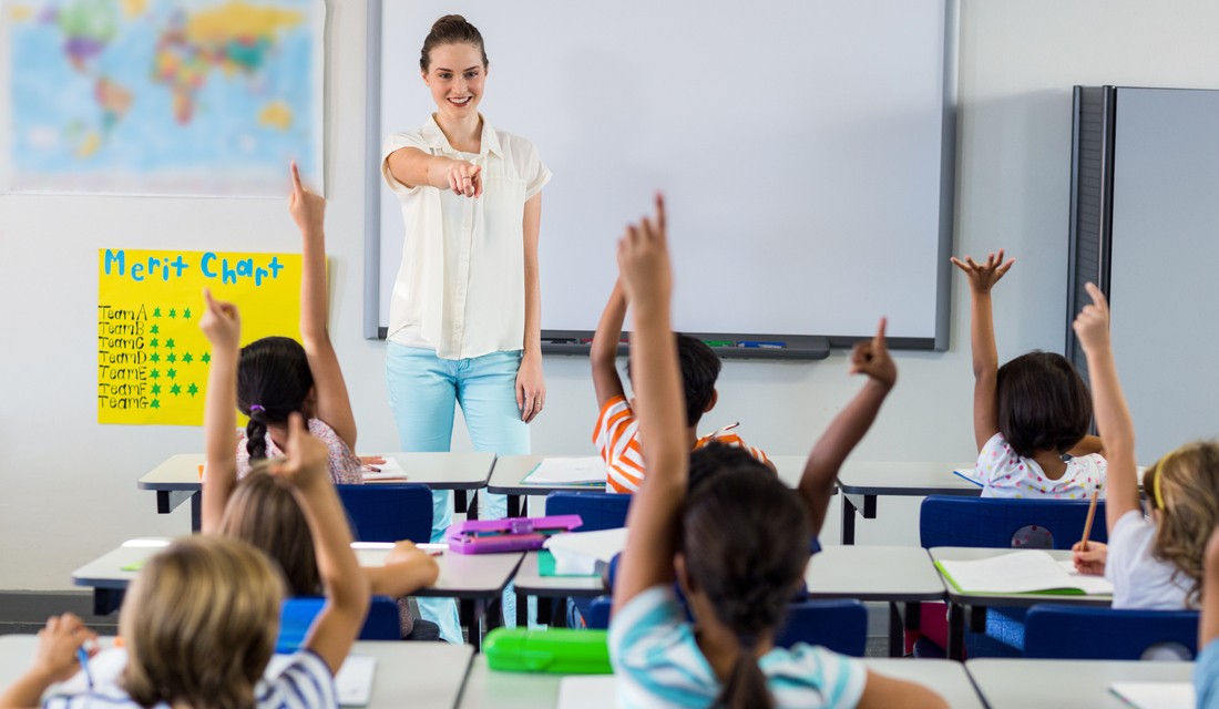 Smiling math teacher pointing students with raised hands in math classroom
