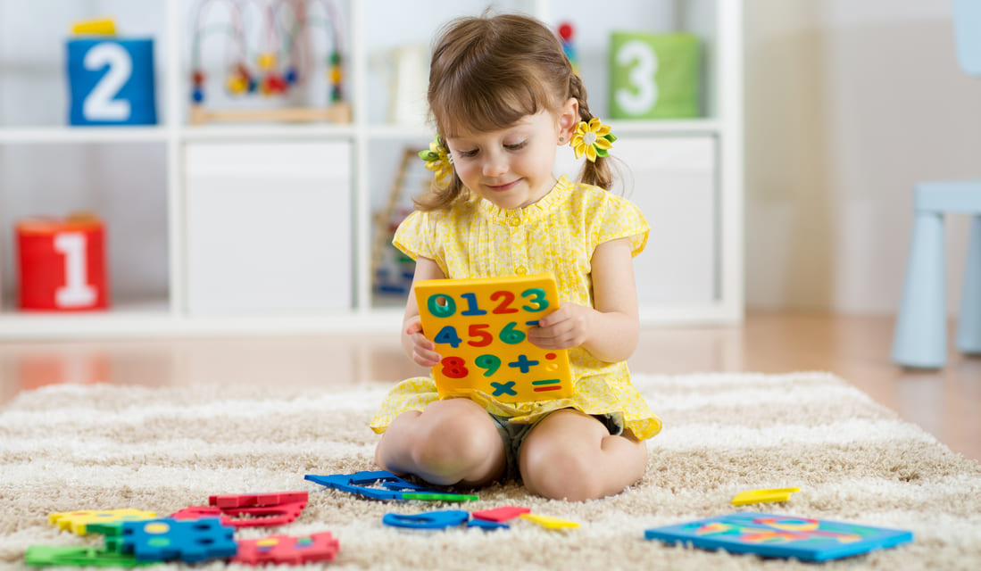 Little girl child playing with lots of colorful plastic digits or numbers on floor indoors.