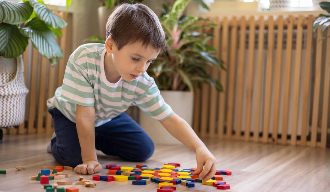 A young boy joyfully stacking colorful wooden blocks on a table, showcasing creativity and playfulness.