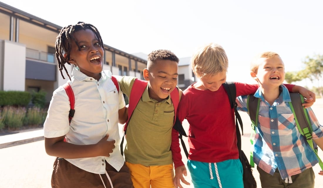 Four children stand together, smiling brightly at the camera, showcasing their joy and friendship.