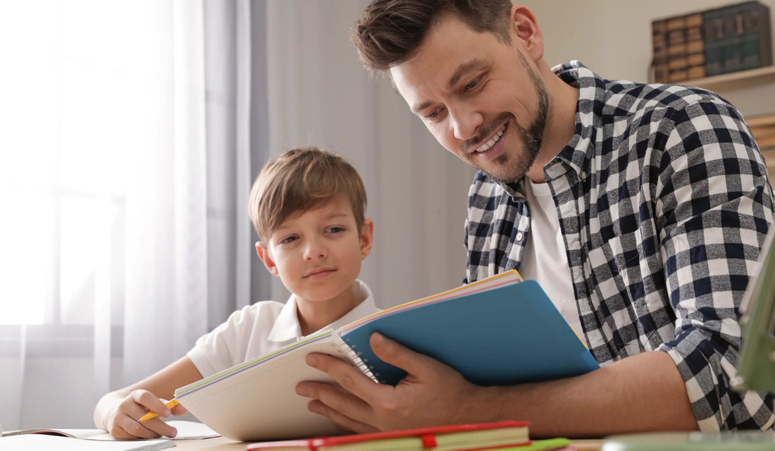 A man and a boy sit at a table, engaged in reading a book together, sharing knowledge and bonding.