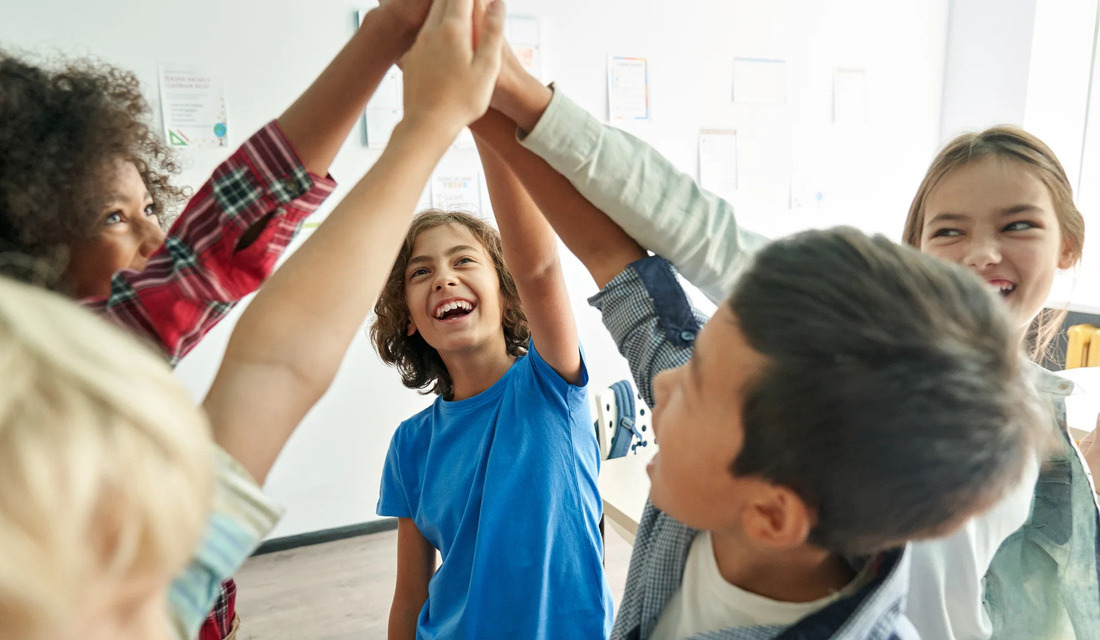 A group of children standing in a circle, holding hands and smiling at each other in a joyful gathering.