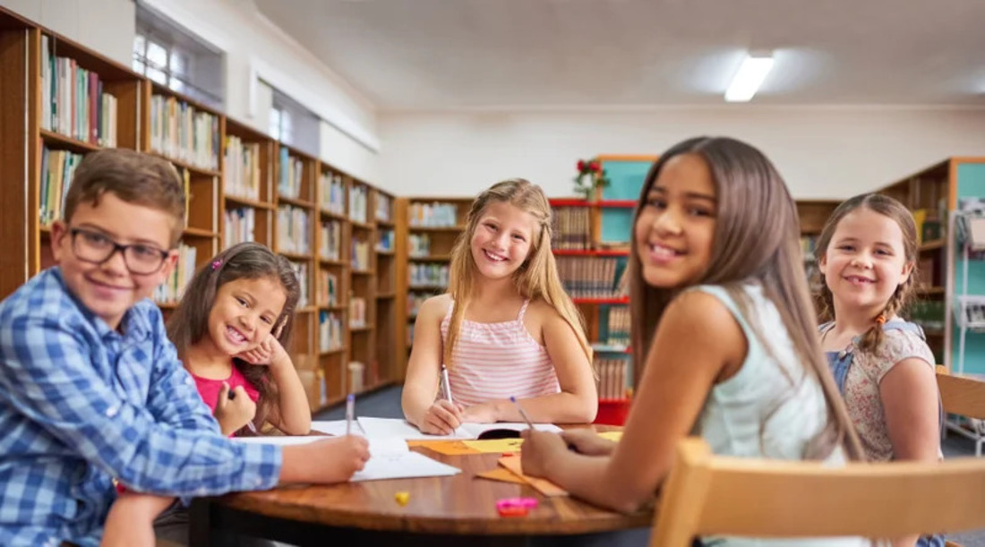 Children engaged in reading and discussing books at a table in a library setting.